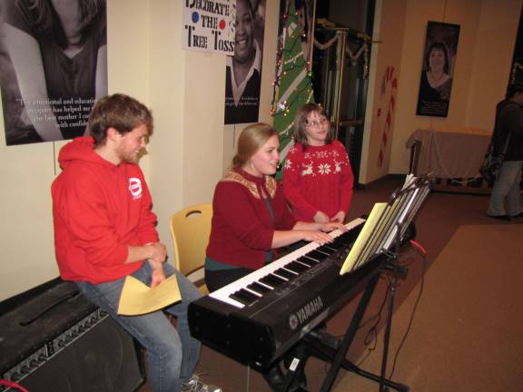 Lizzie Sliker joins volunteer pianist Anna David and her brother, Joe, in a sing-a-long of holiday carols.