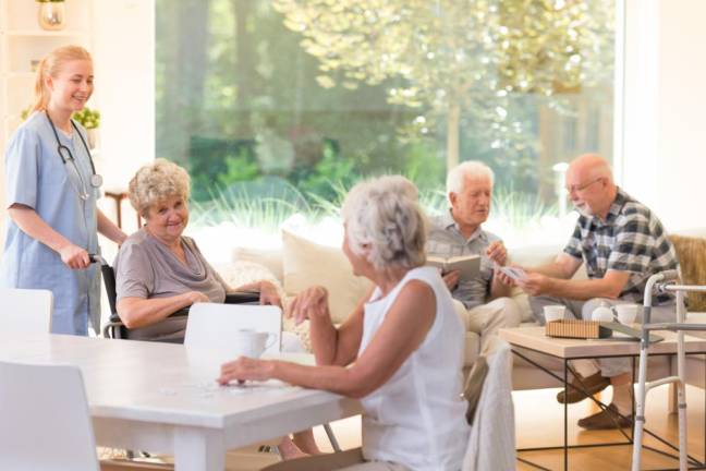 Group of seniors spending free time in bright living room with big window at nursing house