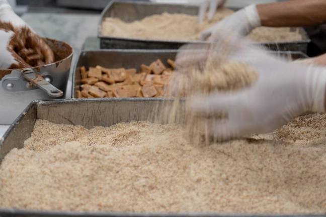 Chocolatiers coating a batch of freshly made buttercrunch candies in roasted almond shavings.