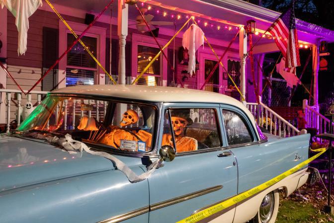 $!<b>“Just married,” a skeleton couple sit in their classic car outside the house marked off with caution tape. (Photo by Aja Brandt)</b>